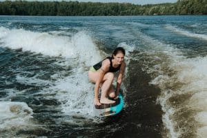 Woman crouching on a wakesurf board, surfing waves on a sunny day.